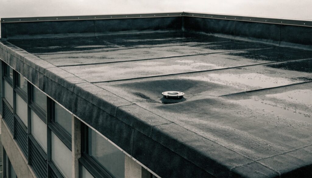 A flat roof covered with a dark single-ply rubber membrane, with a parapet upstand and a rainwater outlet